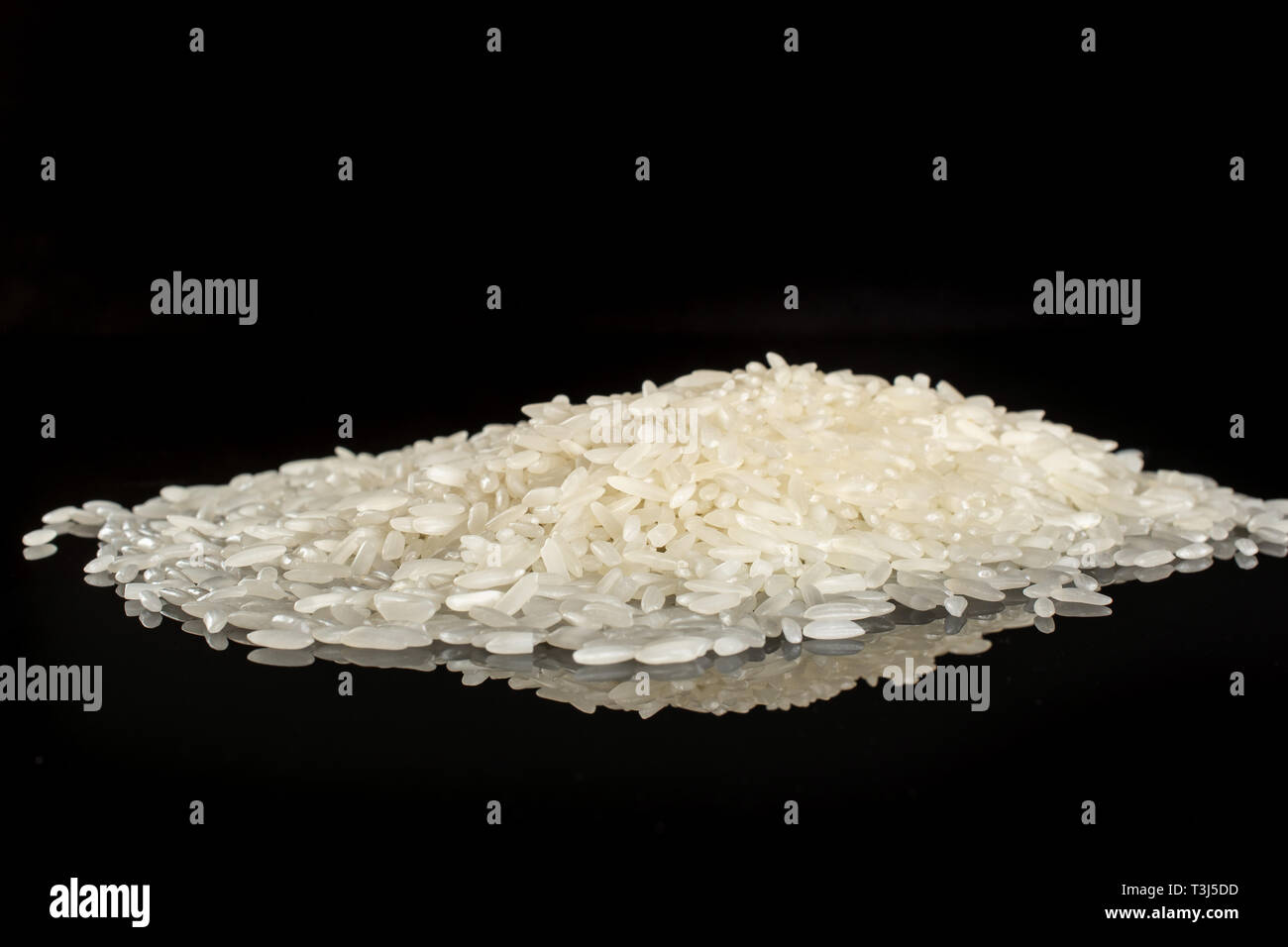 Lot of whole white jasmine rice grains heap isolated on black glass