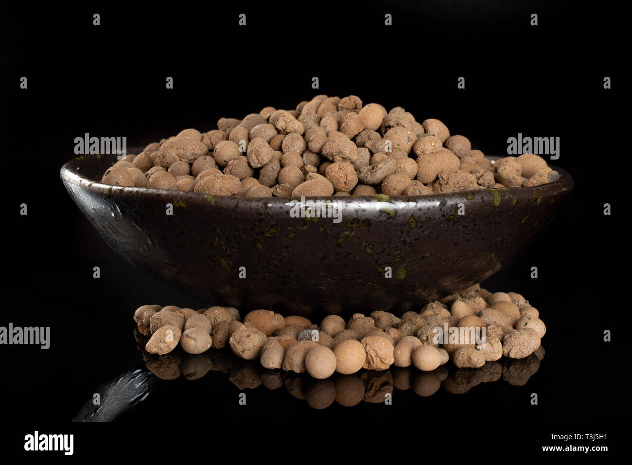 Lot of whole brown clay pebbles (leca) on grey ceramic plate isolated