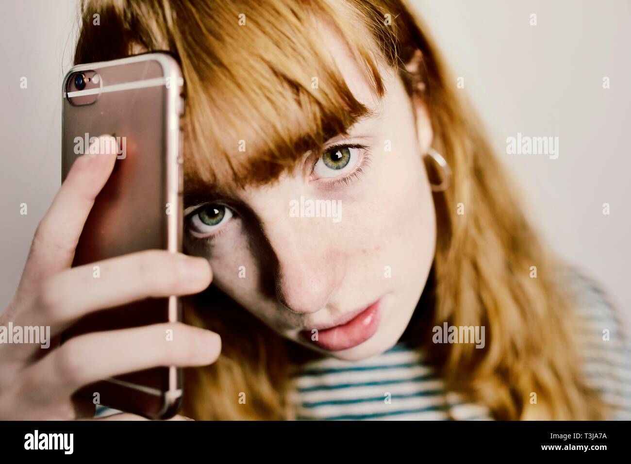 Girl, teenager, red-haired, holds annoyed smartphone to head, studio shot, Germany Stock Photo