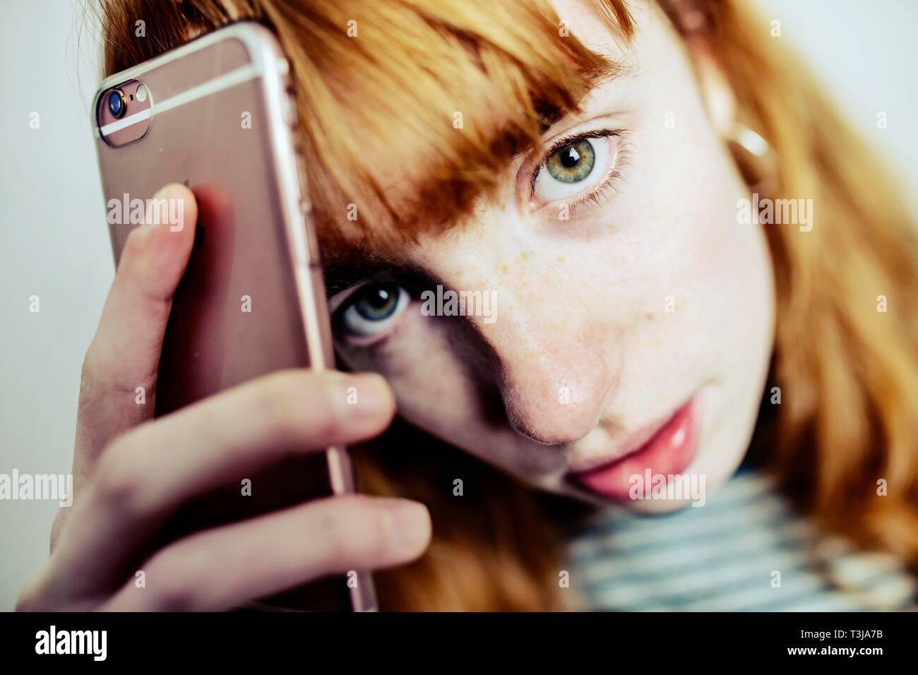 Girl, teenager, red-haired, holds annoyed smartphone to head, studio shot, Germany Stock Photo