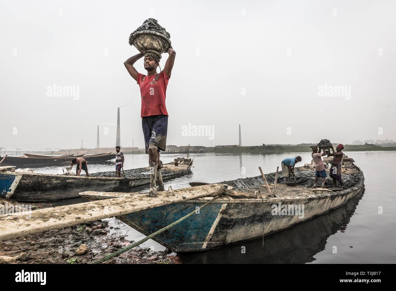 Workers unload clay from a boat, Dhaka, Bangladesh Stock Photo