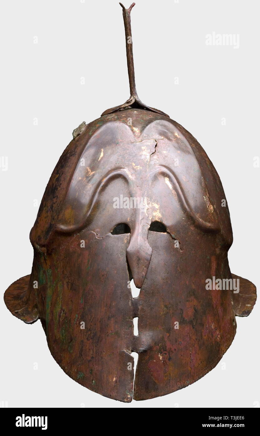 An Apulian-Corinthian helmet, 5th century B.C. A large bronze, clearly set off skull, moulded forehead area, small eye slits, projecting nose-guard, the cheekpieces connected by two bridges. Broad flaring neck-guard. Three holes on the sides for the chinstrap attachment. The helmet rim and centrak face area are decorated with a fishbone pattern. The soldered plume holder is separated at the base and a pair of rivets and other holes in the region of the side mounted plume holders attest to numerous ancient repairs. Total height 26 cm. Weight 949 g, Additional-Rights-Clearance-Info-Not-Available Stock Photo