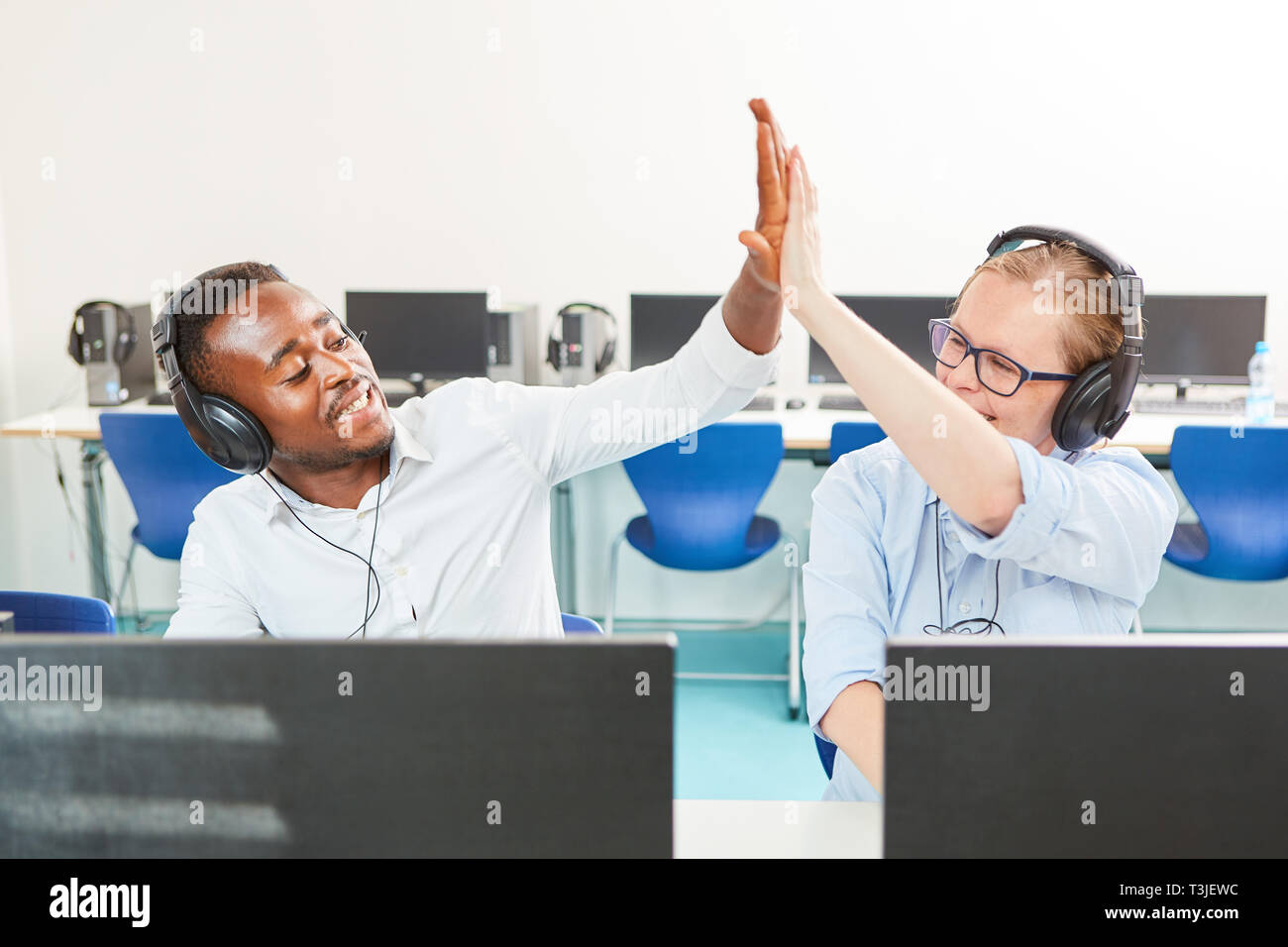 Two students with headphones on the computer in start-up business give themselves a high five Stock Photo