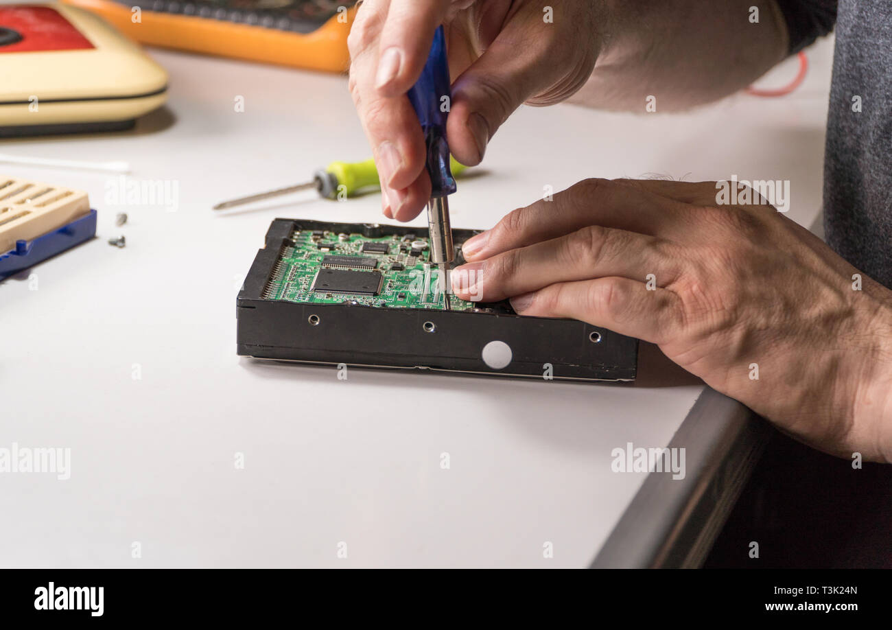 electronic engineer repairs computer hard drive. technologist with a screwdriver disassembles hdd Stock Photo