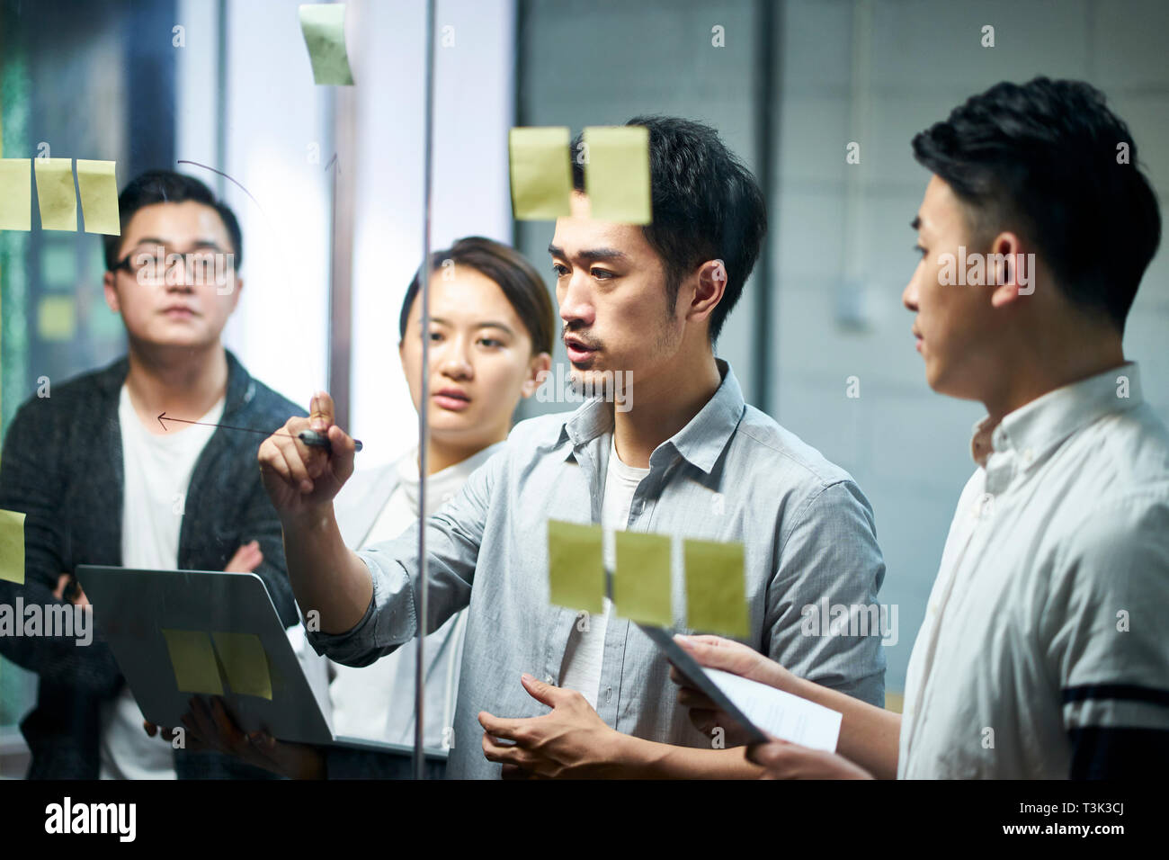 young asian entrepreneur of small company drawing a diagram on glass during team meeting discussing and analyzing business situation in office. Stock Photo