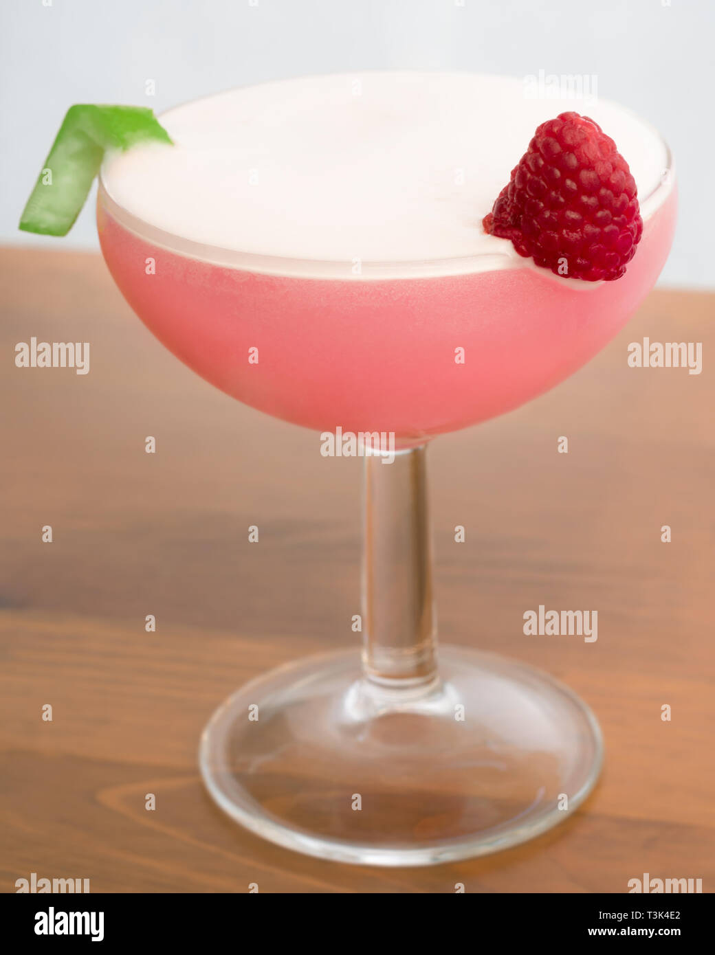 A Clover Club Cocktail in a coupe glass garnished with a raspberry and a lime twist Stock Photo