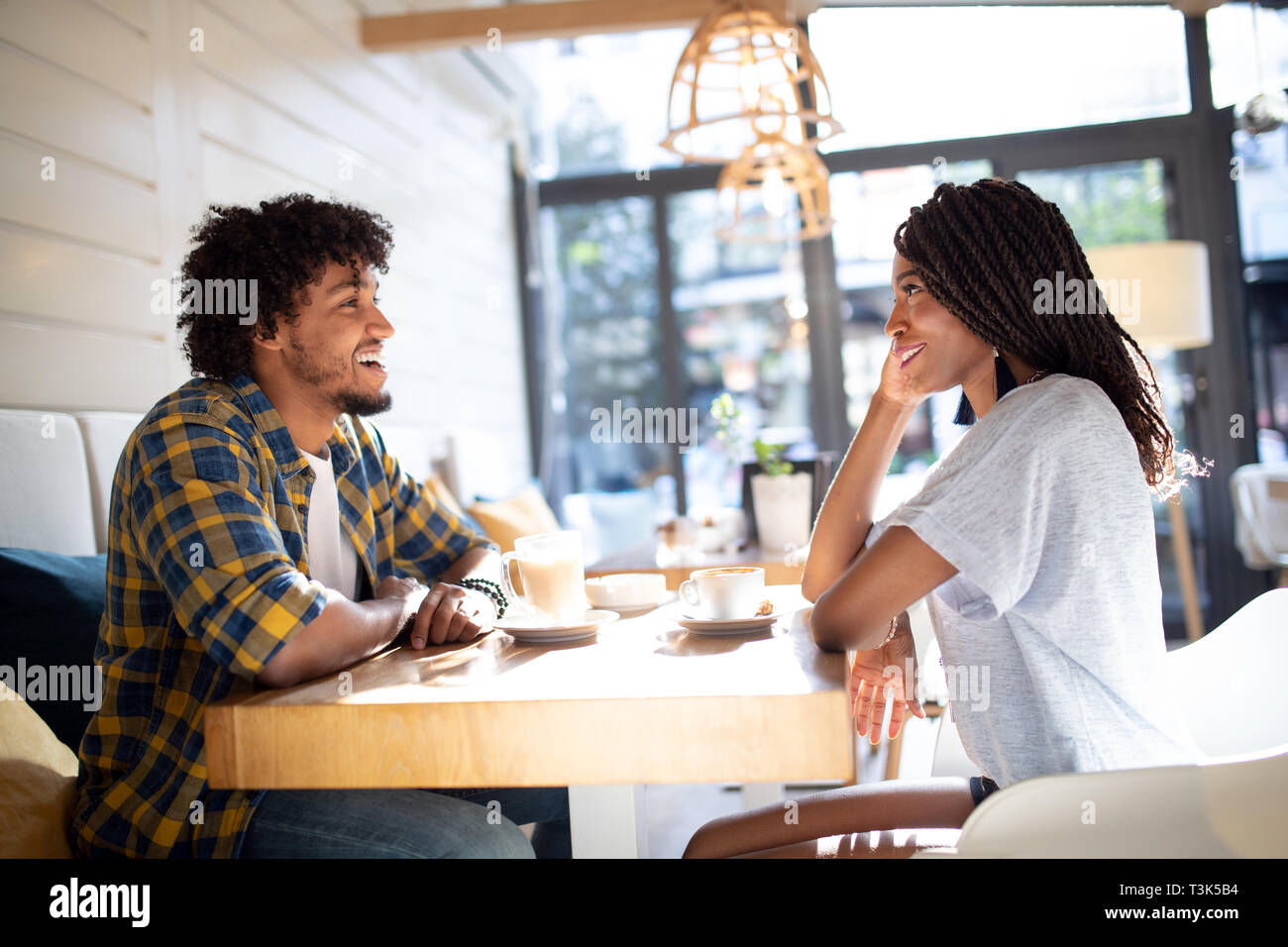 Smiling young african couple sitting at a table at a cafe drinking ...