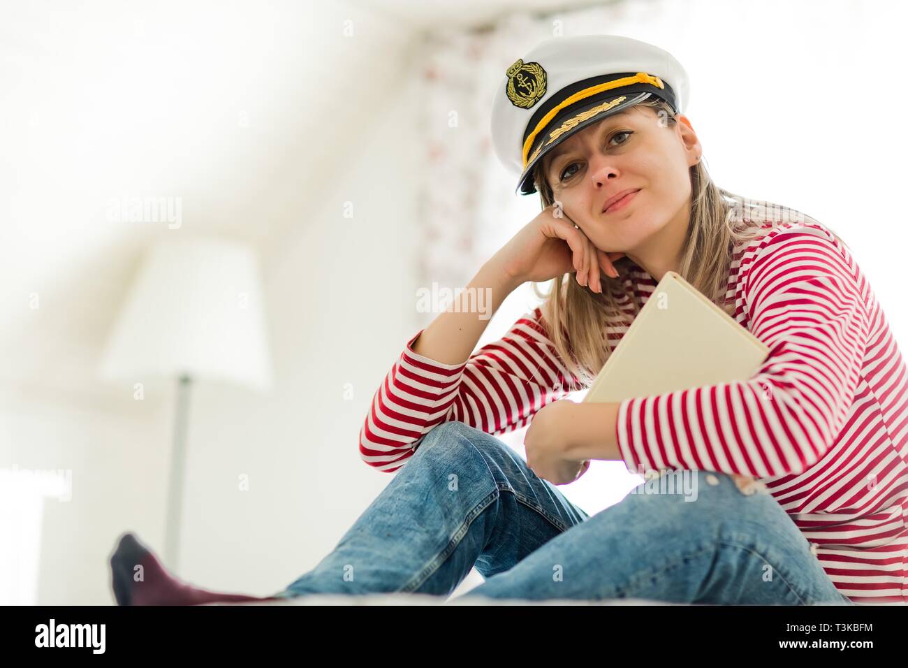 Young woman sailor in captain cap and book, wearing red gaps dress. Stock Photo