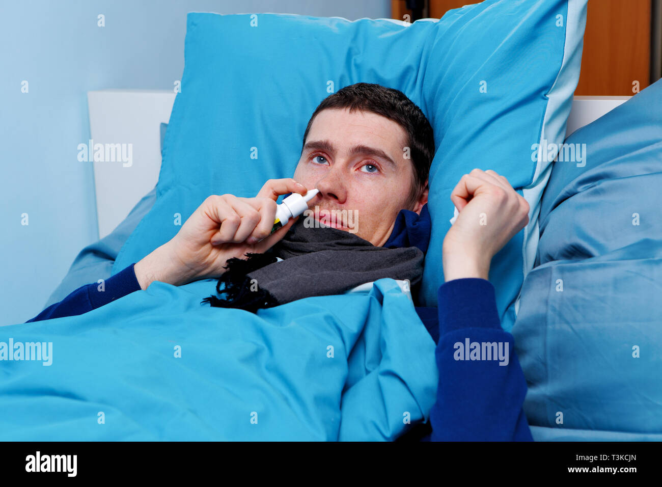 Image of sick man using nasal spray while lying in bed Stock Photo