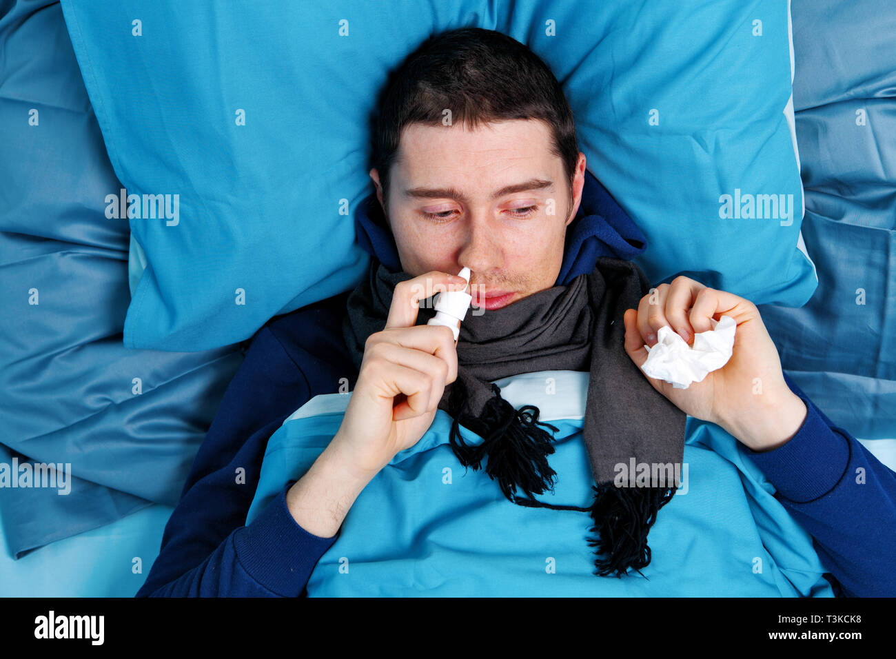 Sick brunet man using nasal spray while lying in bed Stock Photo