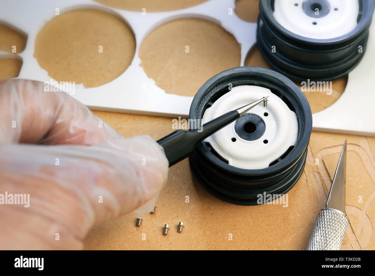 Assembly of a handmade toy part, using precise tweezers tools and gloves to place small screw into thread. Stock Photo