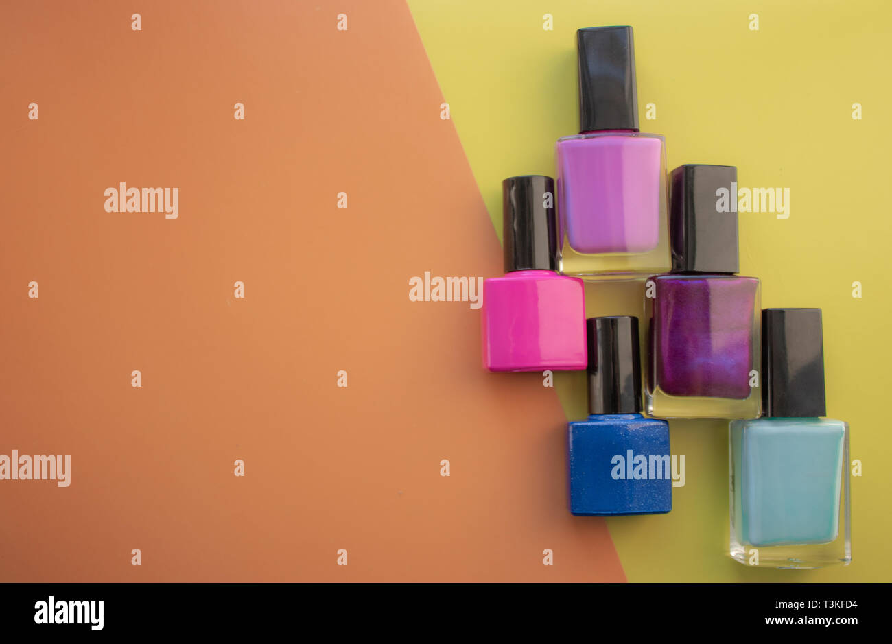 Bottles of nail polish. A group of bright nail polishes on a colored, yellow background. With empty space on the left. View from above Stock Photo