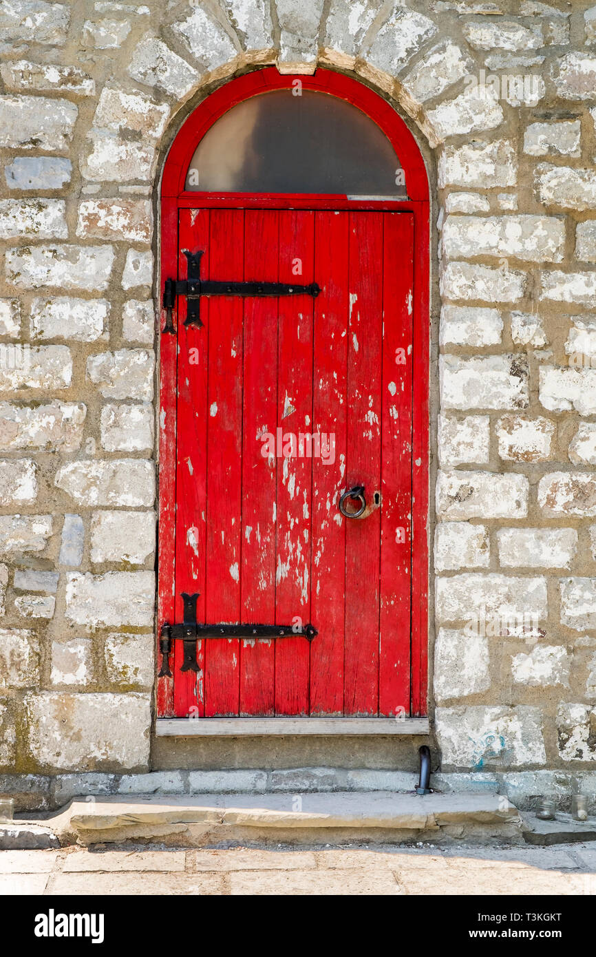 A red arched top door with peeling paint black hinges and handle at the entrance to Gibraltar Paint Lighthouse on Toronto Island's in Toronto Canada. Stock Photo