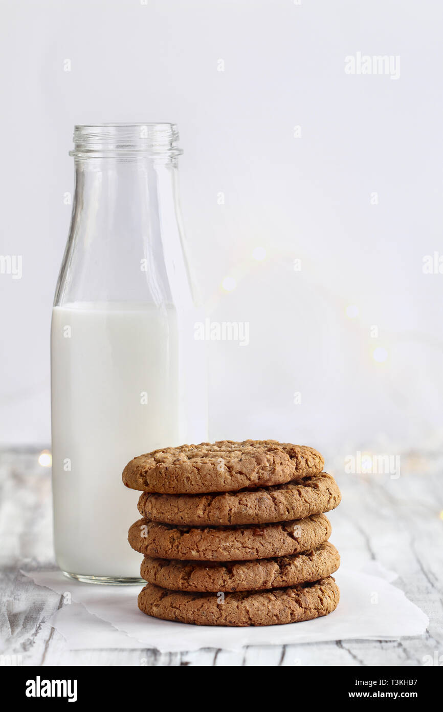 Stack of fresh homemade oatmeal cookies with a bottle of milk on a white table against a white background.. Stock Photo