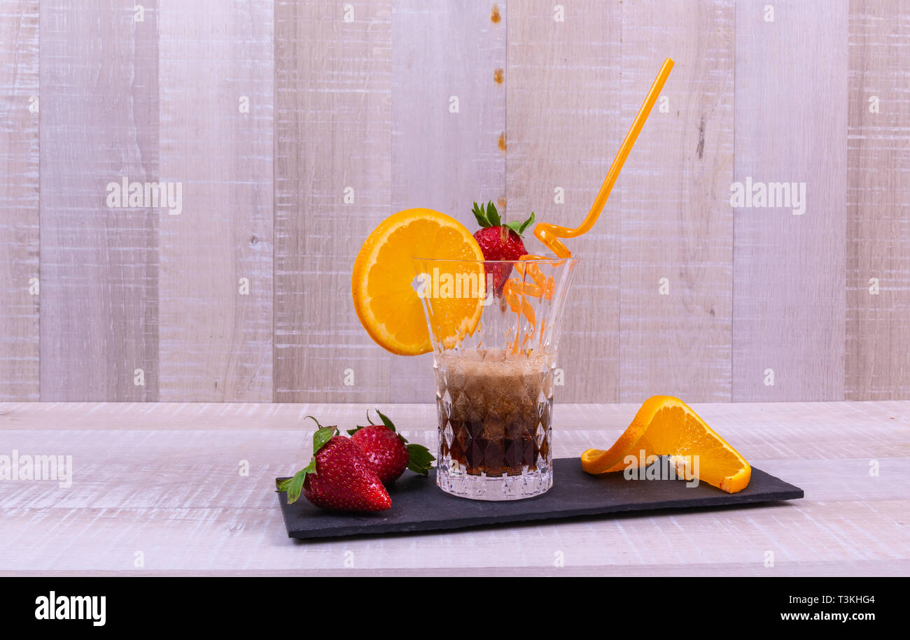 cola pouring into glass , beverage and fruit on a black slate with a light wooden background Stock Photo