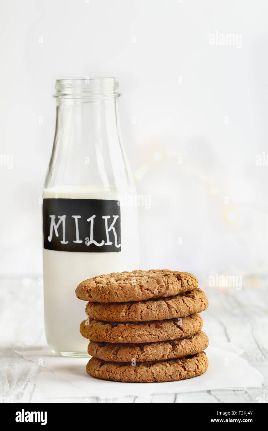 Stack of fresh homemade oatmeal cookies with a bottle of milk on a white table against a white background.. Stock Photo