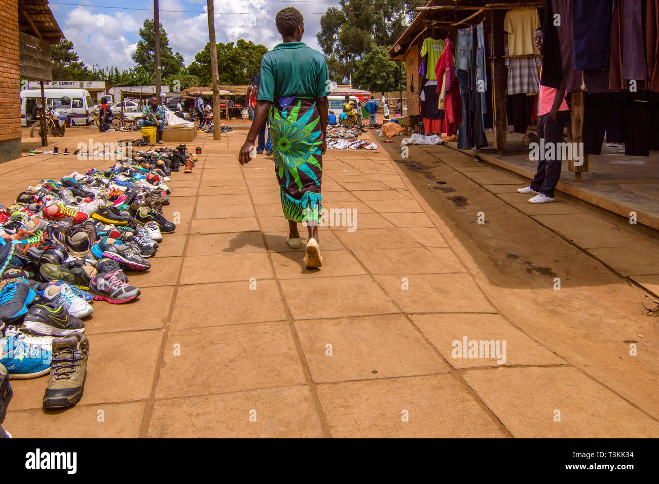 Malawian woman walks past a line of used shoes for sale at Dedza Market Malawi Stock Photo