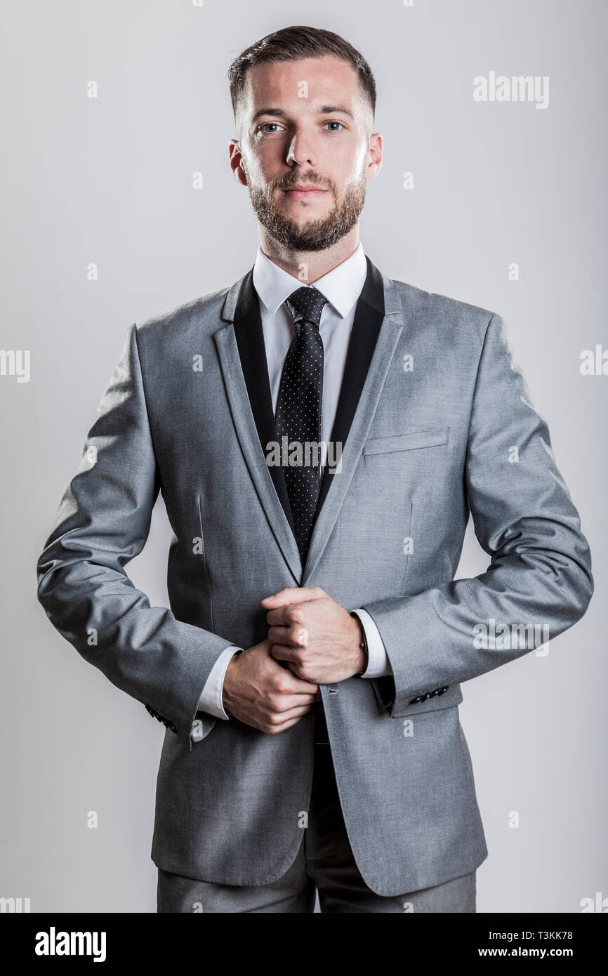 bearded young business man in a silver gray shiny elegant suit with black collar white shirt and black tie Stock Photo