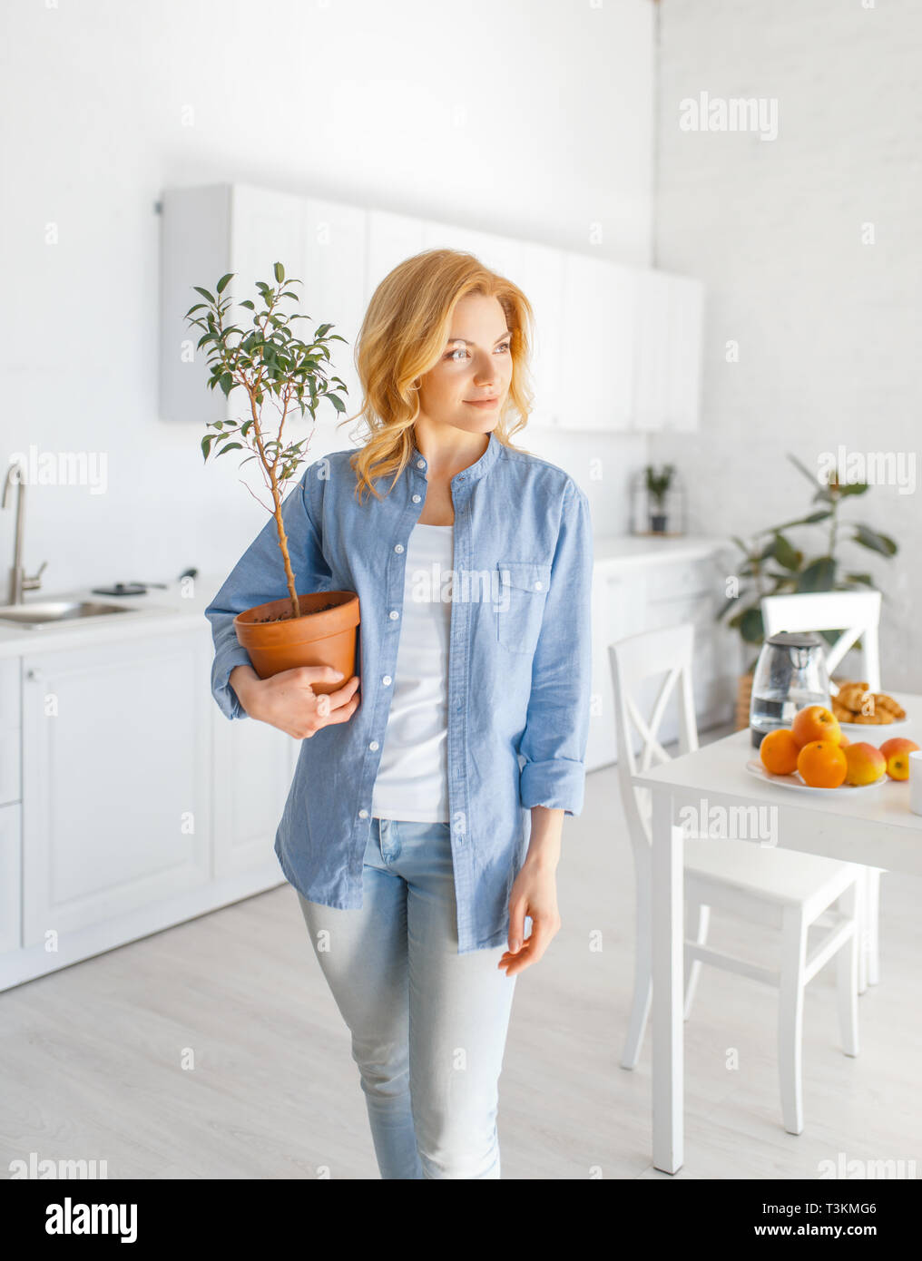 Young woman holds a flower in a pot on the kitchen Stock Photo