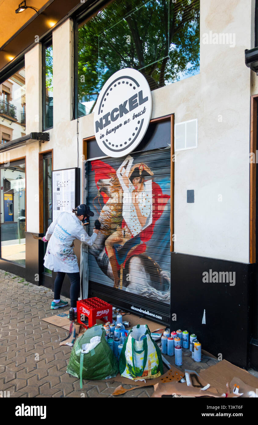 Woman mural artist painting a picture on a restaurant shutter in Seville Stock Photo
