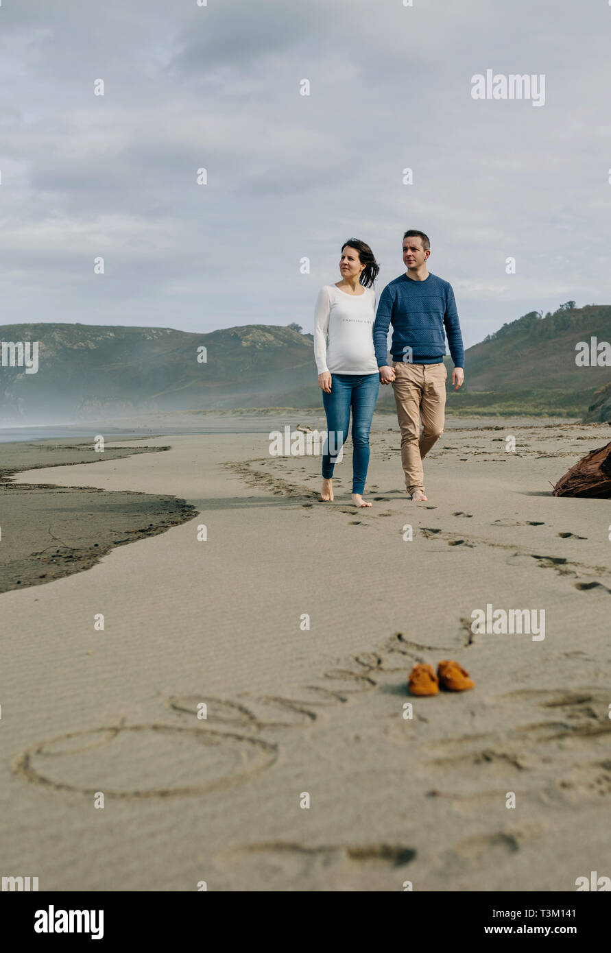 Parents walking with baby name Oliver written in the sand Stock Photo