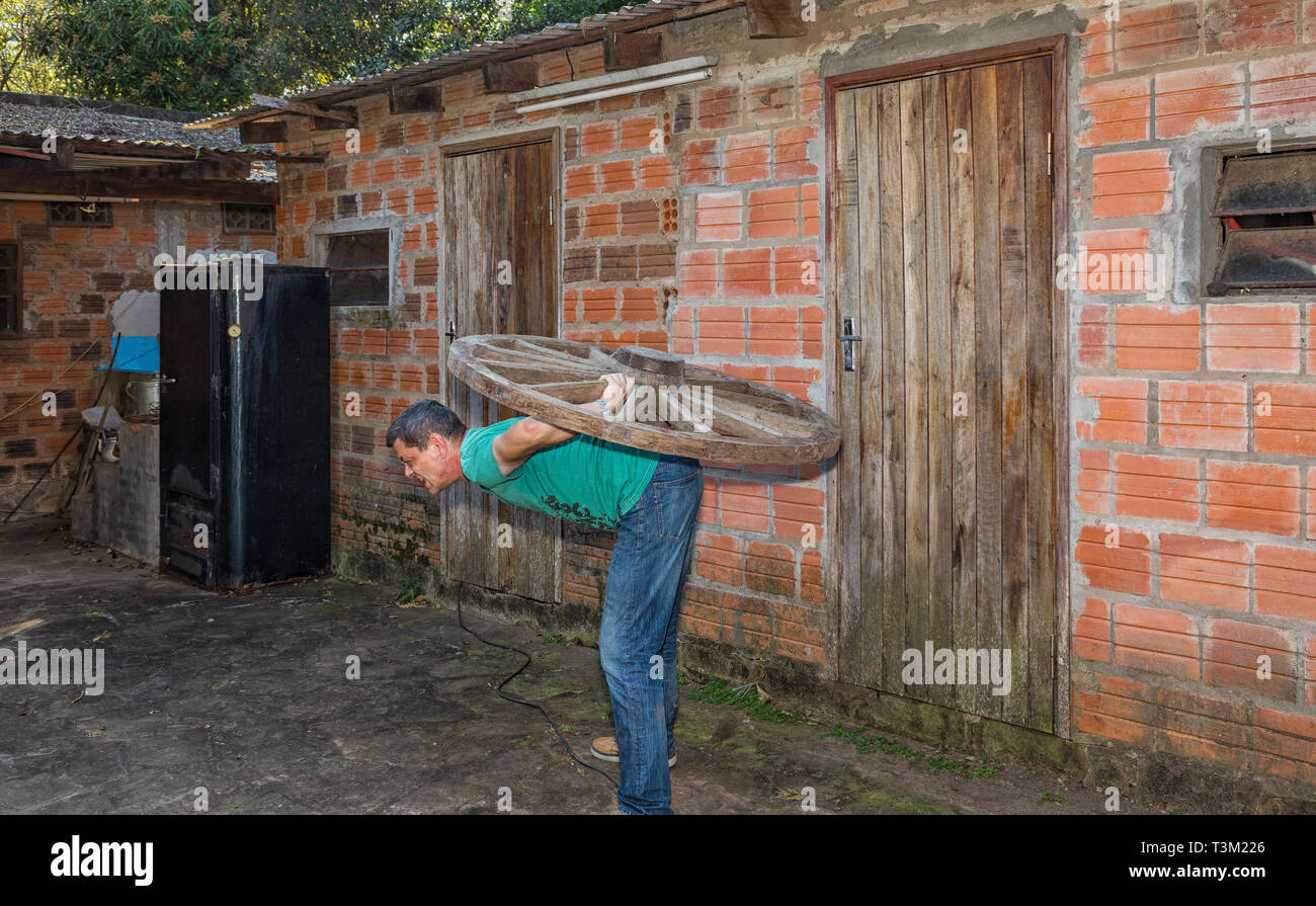 A man carries a wooden wheel on his back. Stock Photo