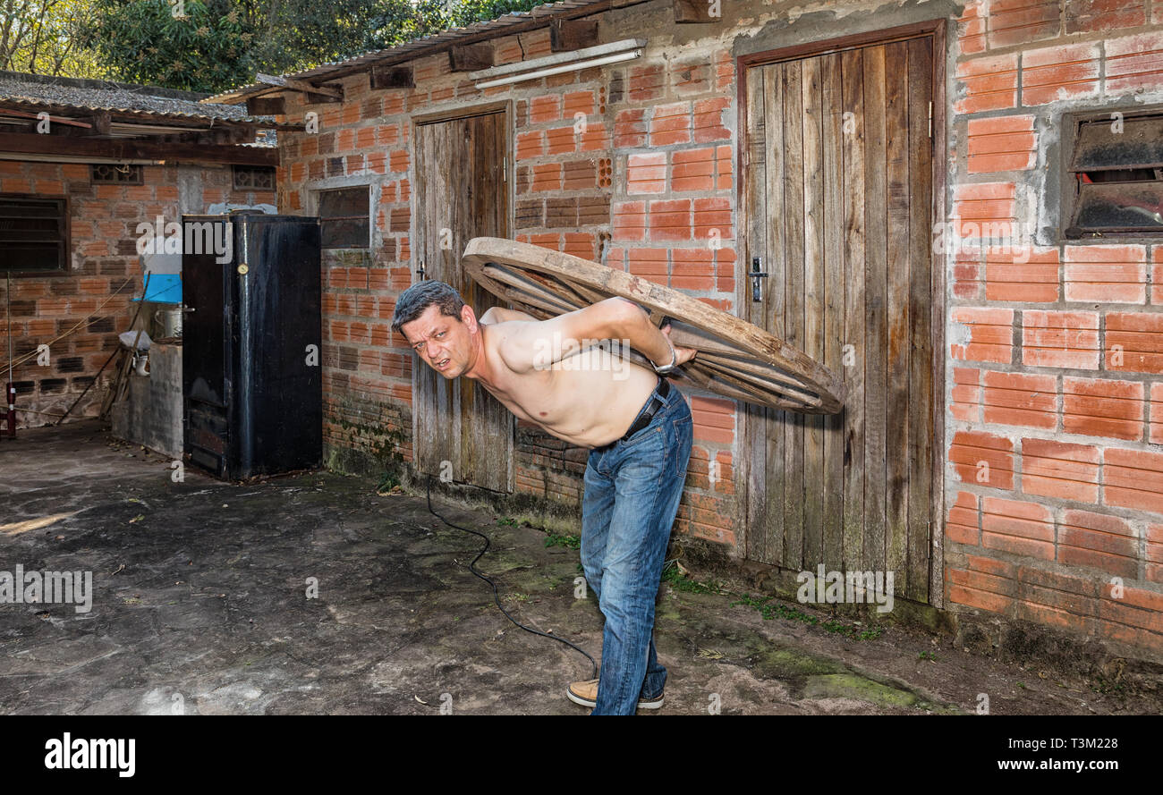 A man carries a wooden wheel on his back. Stock Photo