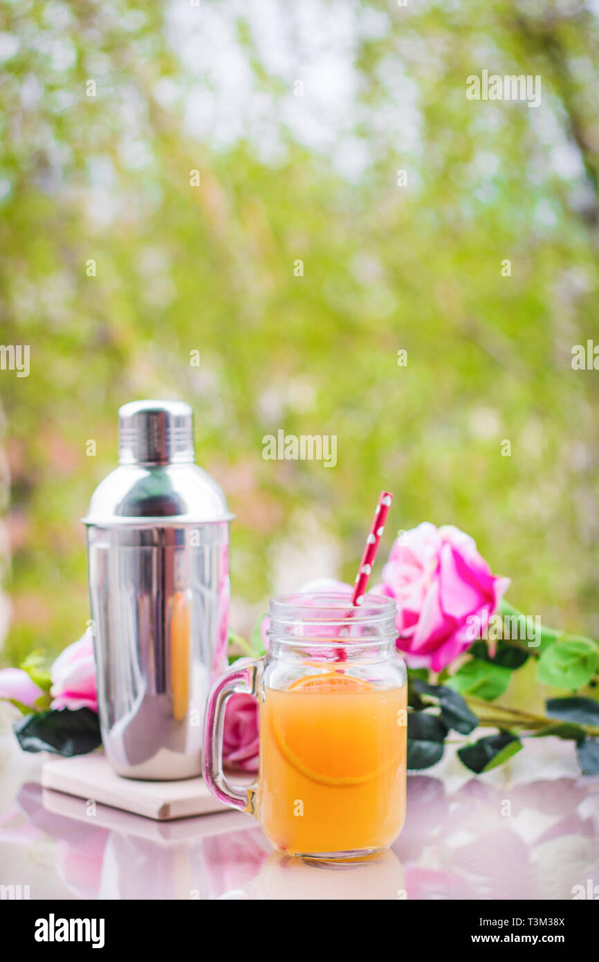 Orange juice cocktail in a glass jar with roses and a shaker Stock