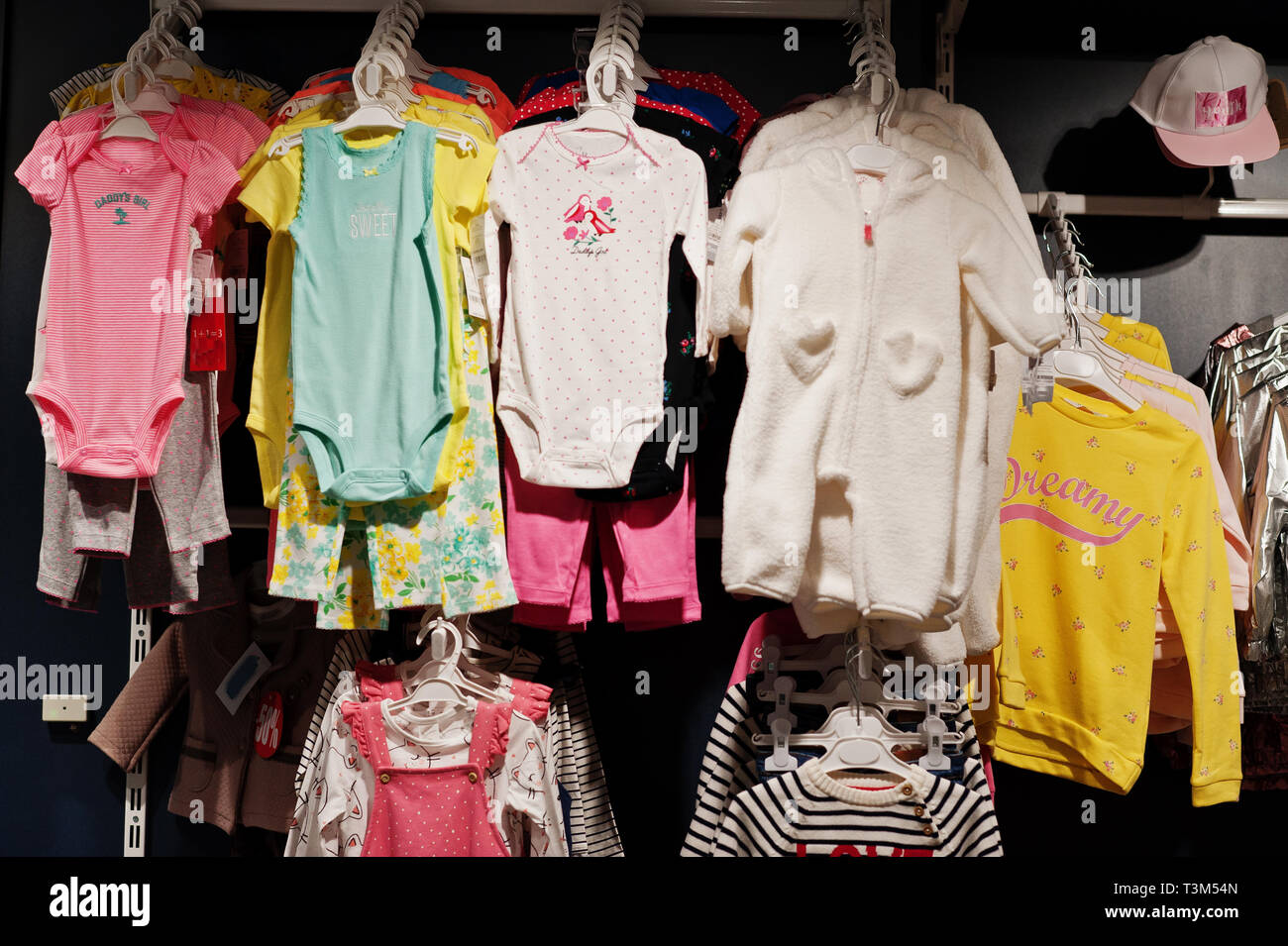 Children's bright clothes hang on the display in the baby clothing store. Girls section. Stock Photo
