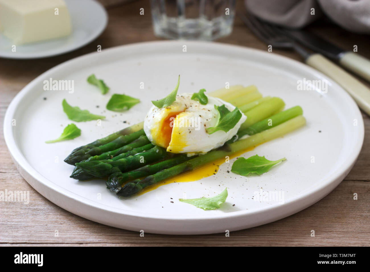 Breakfast consisting of poached egg and boiled asparagus with butter and lettuce on a wooden surface. Rustic style. Stock Photo