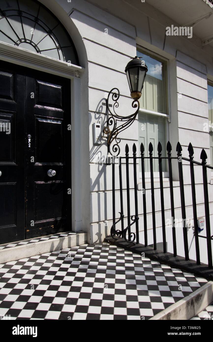 Front door of gentrified London house with black and white tiled entrance step and railings to side Stock Photo