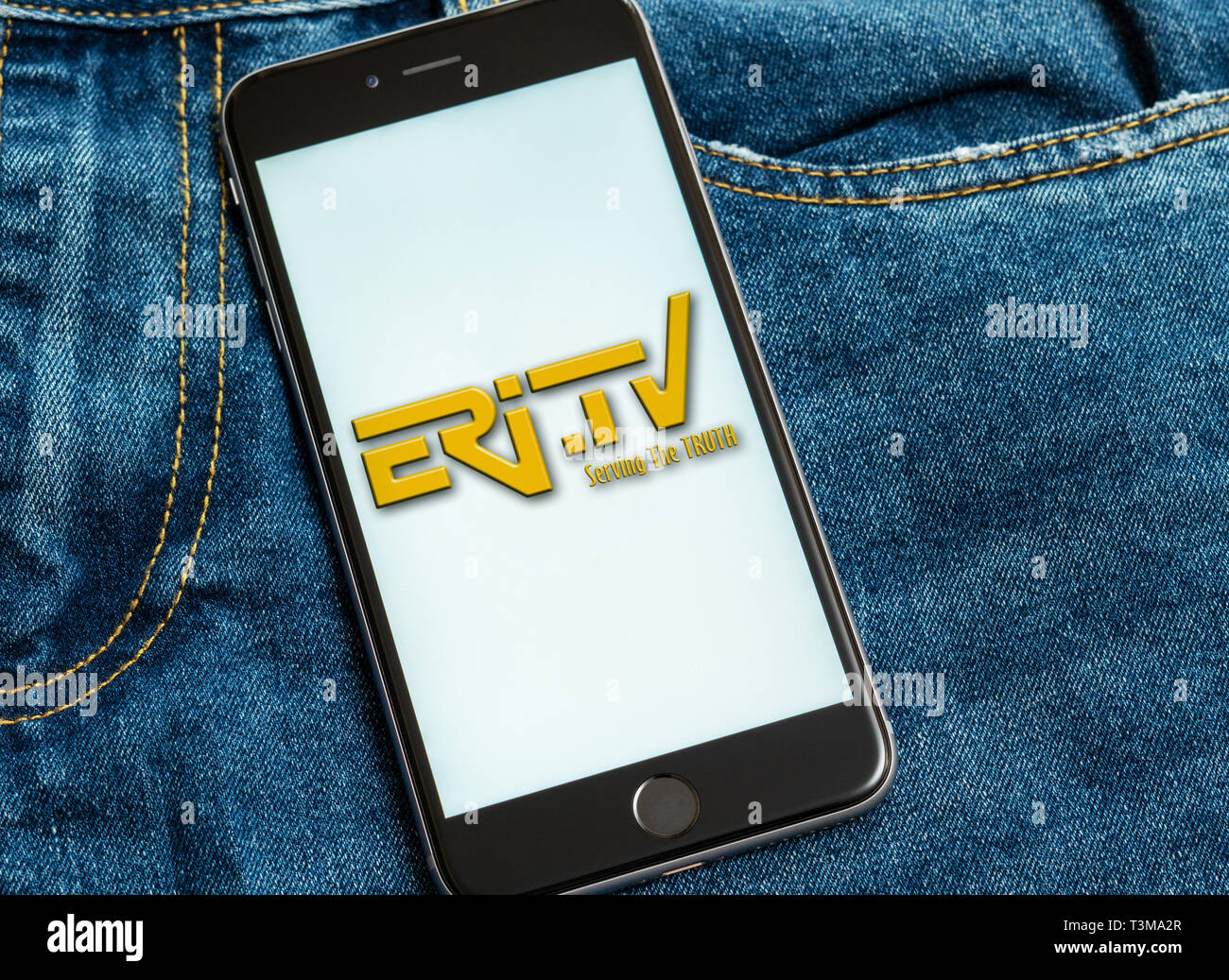 Black phone with logo of news media Eritrean Television (Eri-TV) on the screen. News media icon. Denim jeans background. Can be used as illustrative Stock Photo