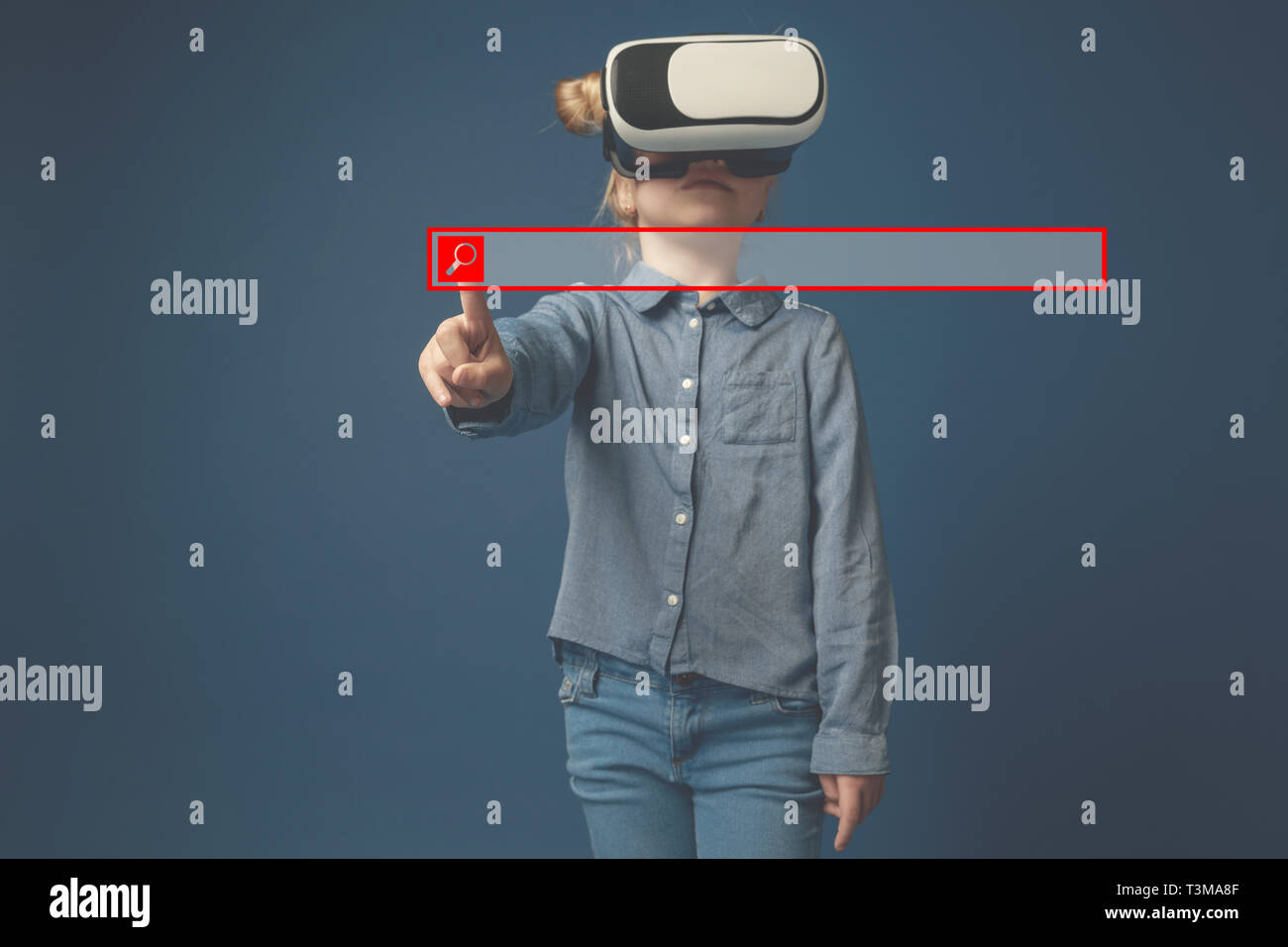 In touch with hi-tech. Little girl or child pointing to the empty search  bar with VR-glasses isolated on blue studio background. Copy space. Concept  of cutting edge technology, video games, innovation Stock