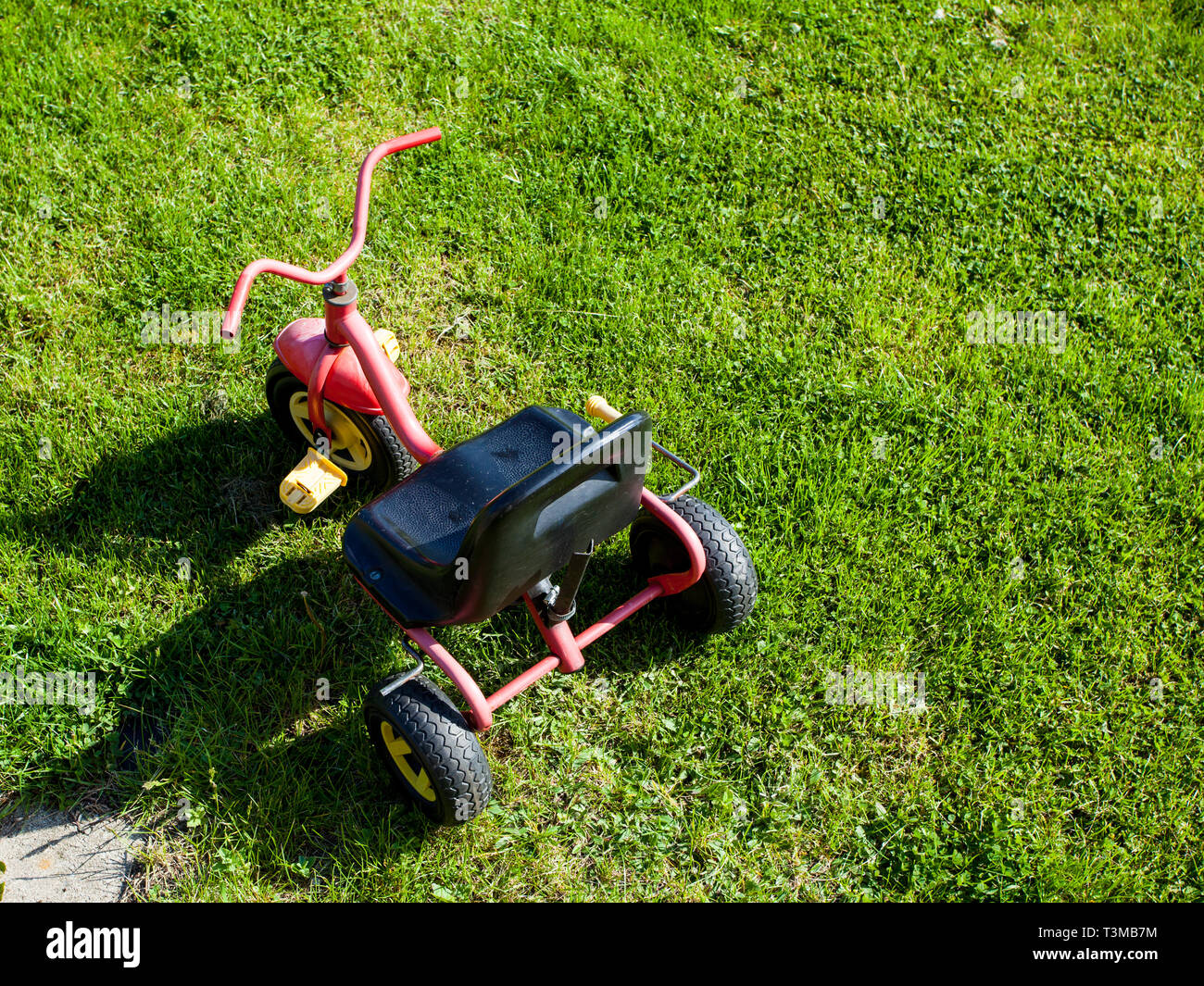 Childhood. Small red tricycle cycle toy on the green grass. Outdoor. Play and learn. Stock Photo