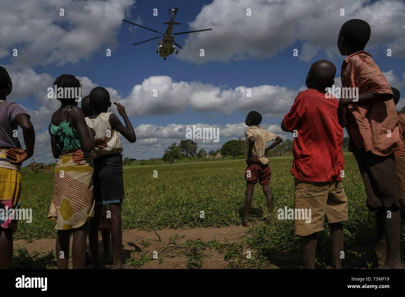 Mozambican children watch a U.S. Air Force helicopter take off after delivering food aid in the aftermath of the massive Cyclone Idai April 8, 2019 in Bebedo, Mozambique. The World Food Programme, with help from the U.S. Air Force is transporting emergency relief supplies to assist the devastated region. Stock Photo