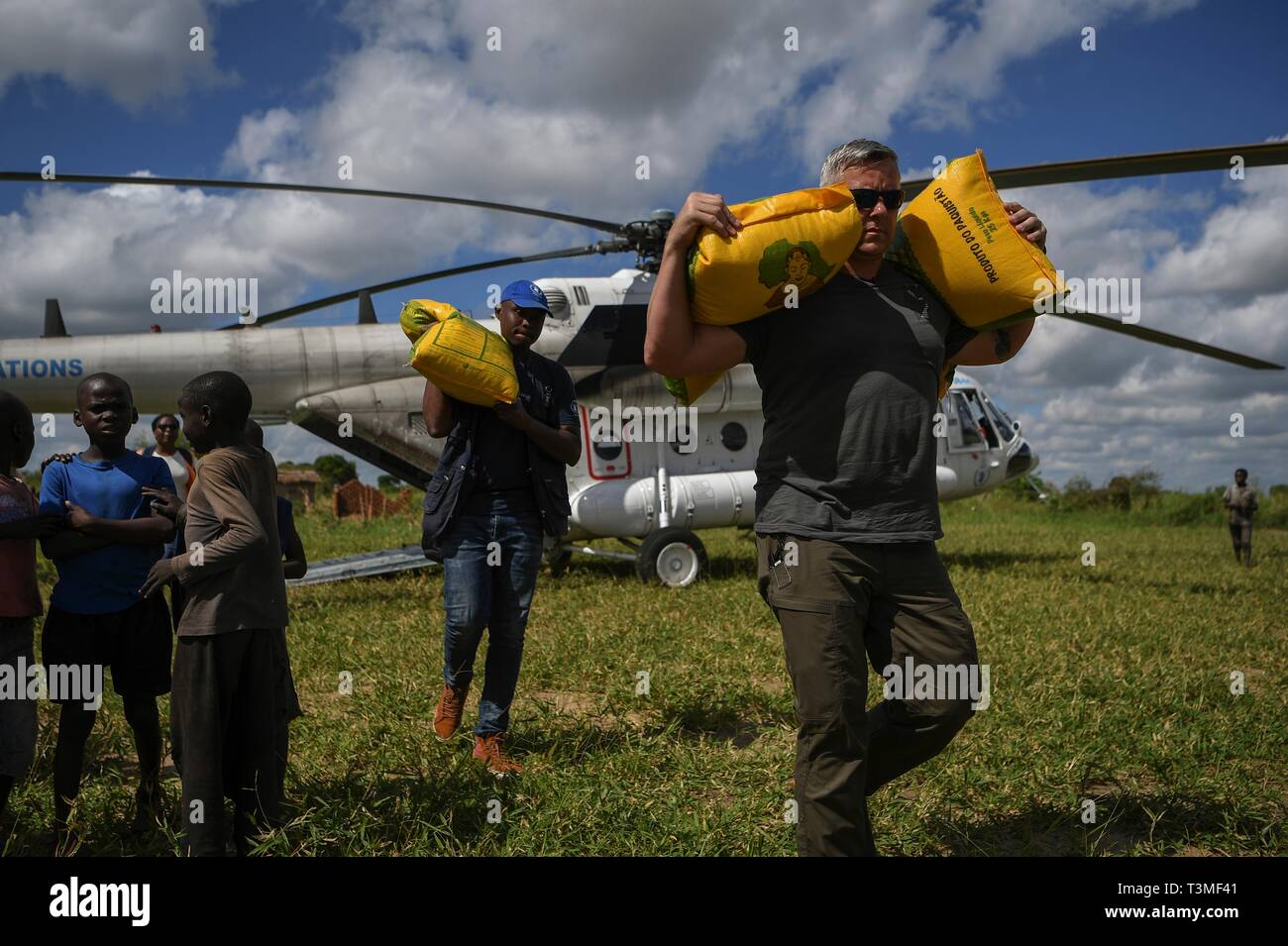 Local volunteers and U.S. service members assist in unloading food aid from a helicopter in the aftermath of the massive Cyclone Idai April 8, 2019 near Bebedo, Mozambique. The World Food Programme, with help from the U.S. Air Force is transporting emergency relief supplies to assist the devastated region. Stock Photo