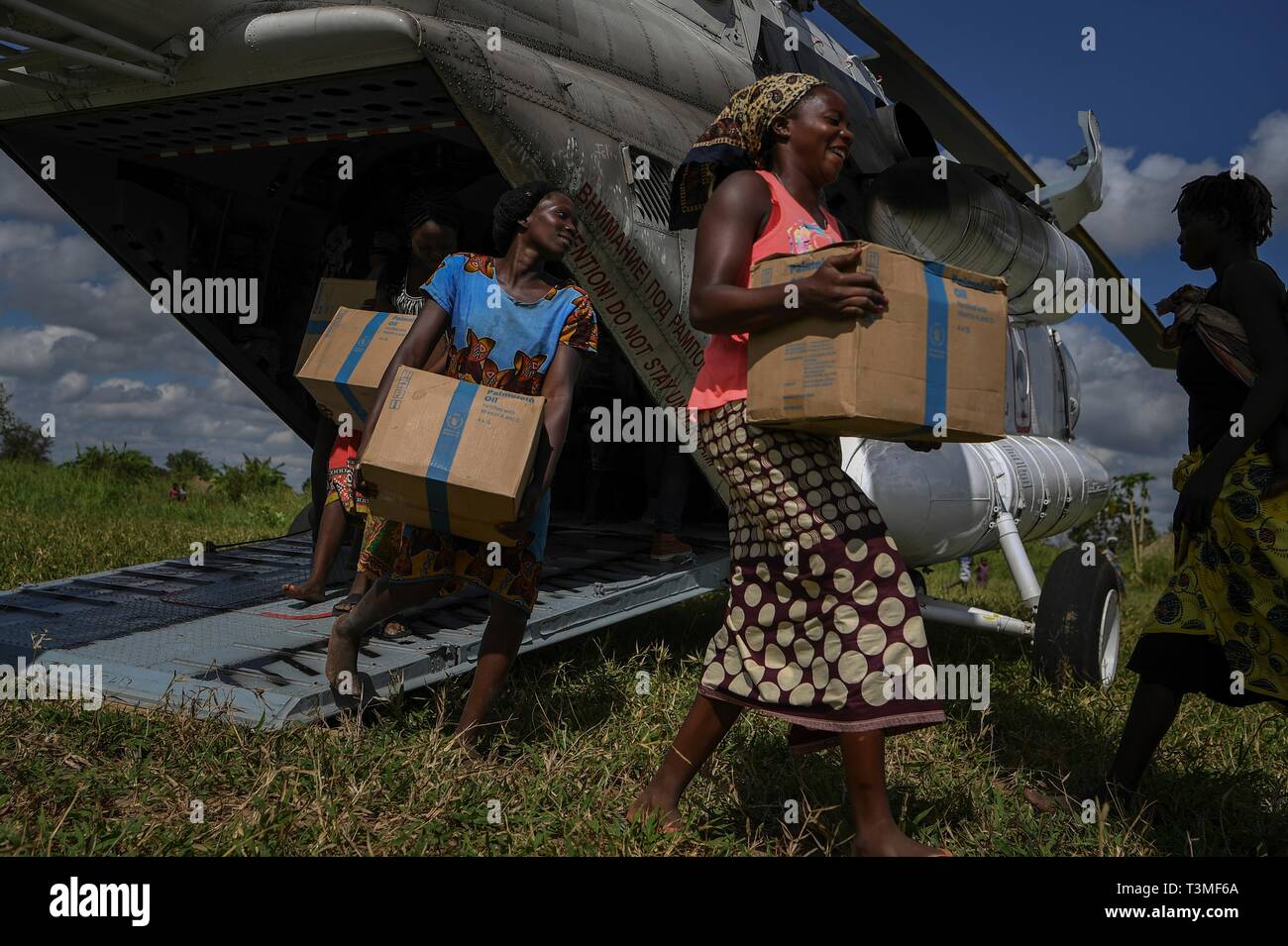 Local volunteers assist in unloading food aid from a helicopter in the aftermath of the massive Cyclone Idai April 8, 2019 in Bebedo, Mozambique. The World Food Programme, with help from the U.S. Air Force is transporting emergency relief supplies to assist the devastated region. Stock Photo