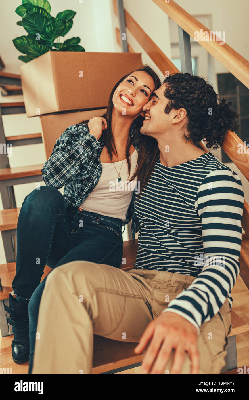 The young couple is moving into a new house. They are sitting on stairs ...