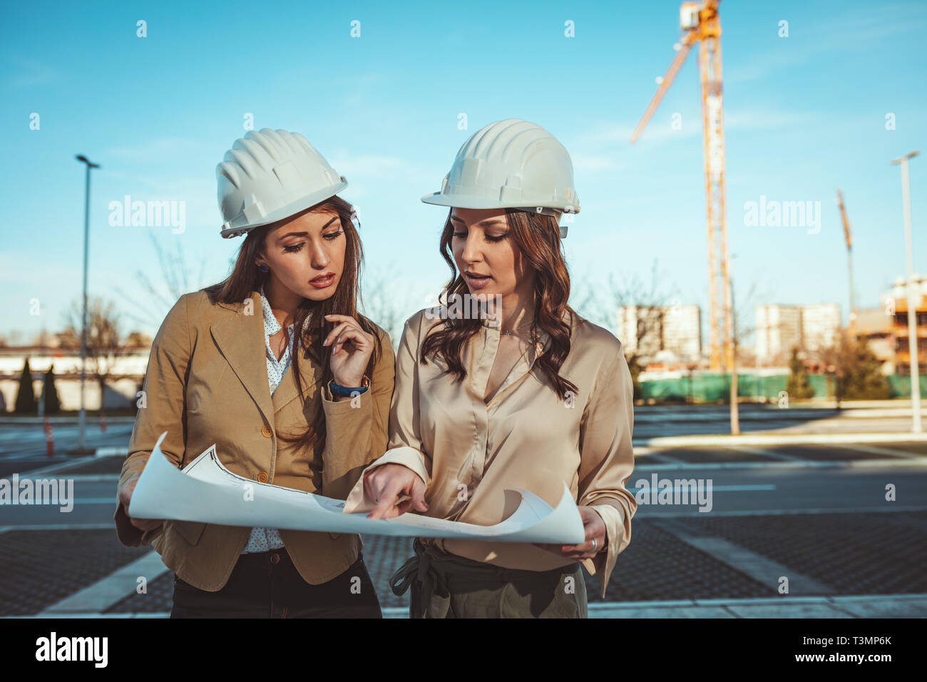 Young successful female engineers with white helmets and blueprints in ...