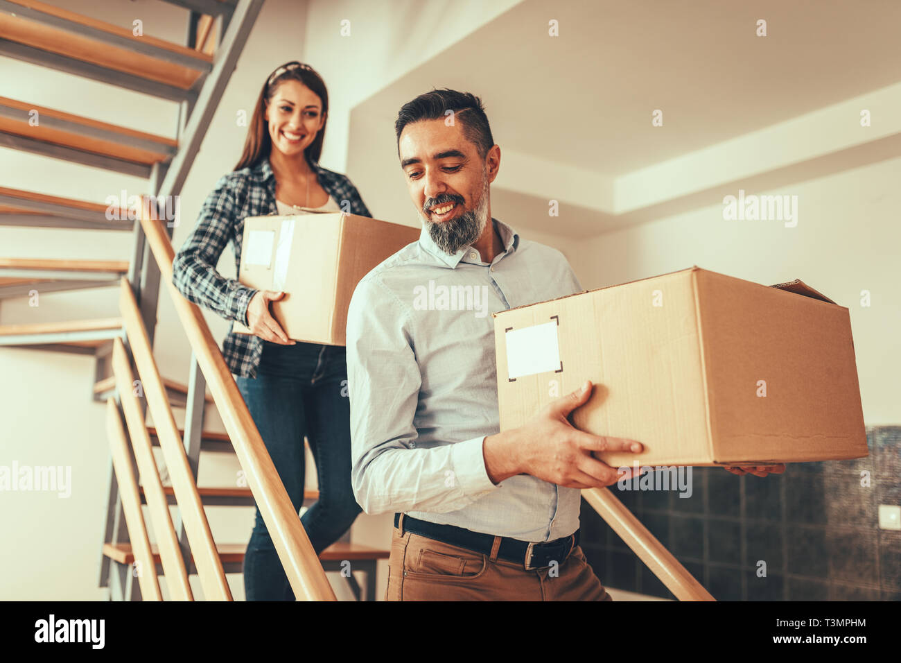 The young happy couple is moving into a new house. They bring boxes ...