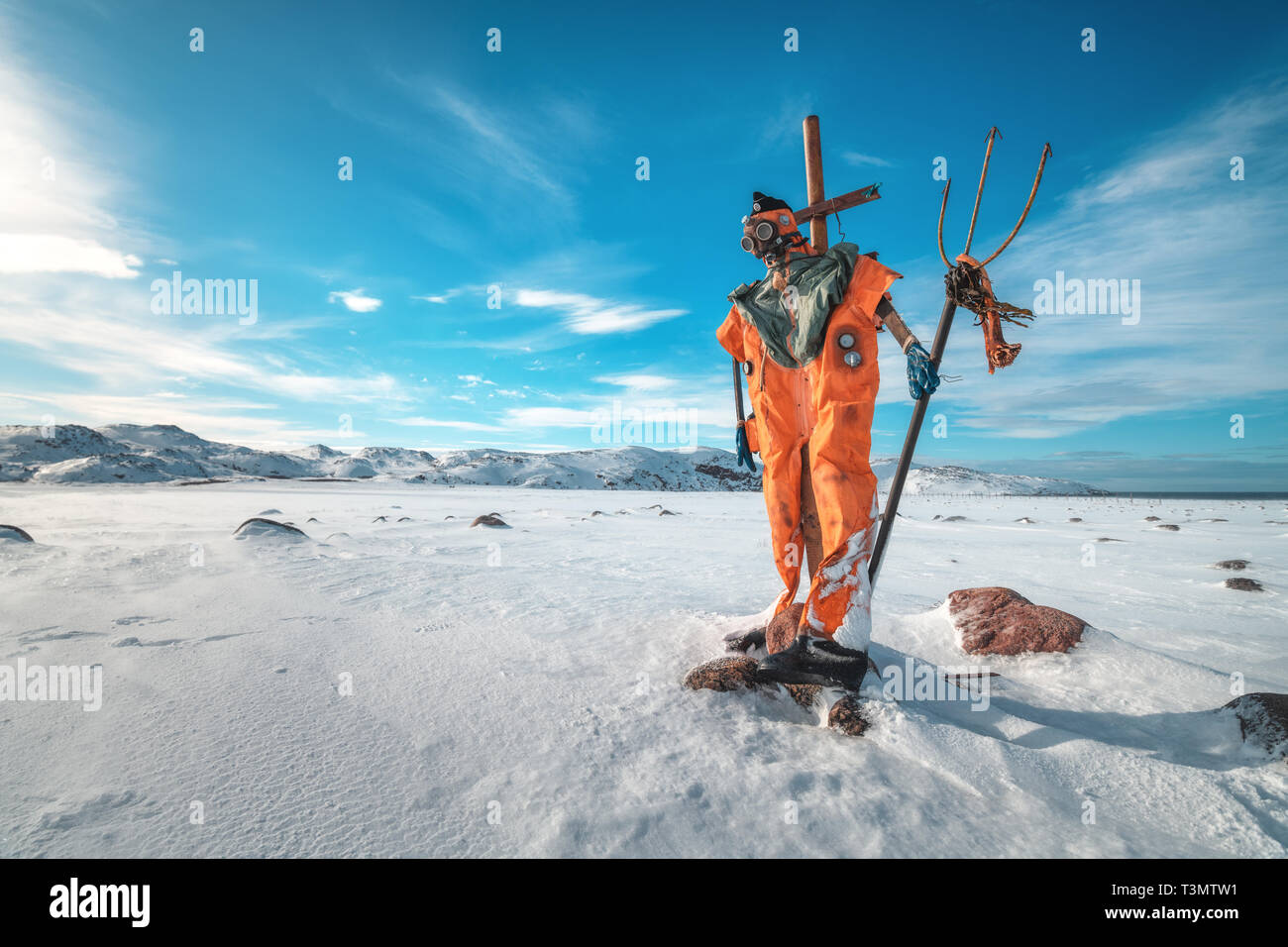 Scarecrow In Orange Clothes And Gas Mask With Trident Is Against Blue Sky With Clouds And Snowy Meadow Winter Landscape With Funny Dummy Stones In S Stock Photo Alamy