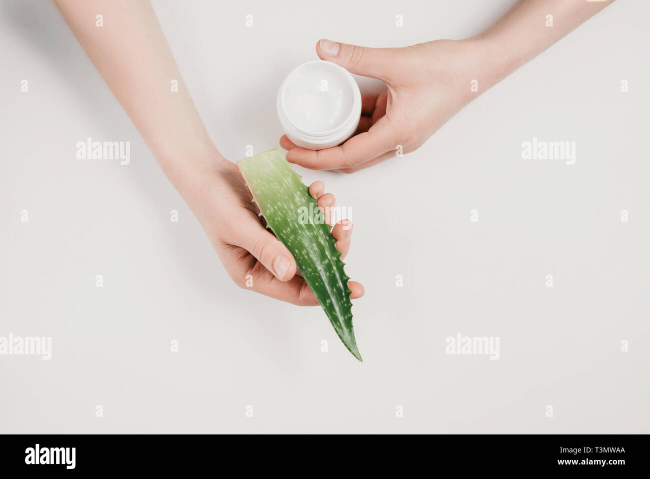 Closeup of beautiful female hand with cosmetic cream and aloe vera leaf on white background. Flat lay, top view, copy space, minimal style. Beauty con Stock Photo