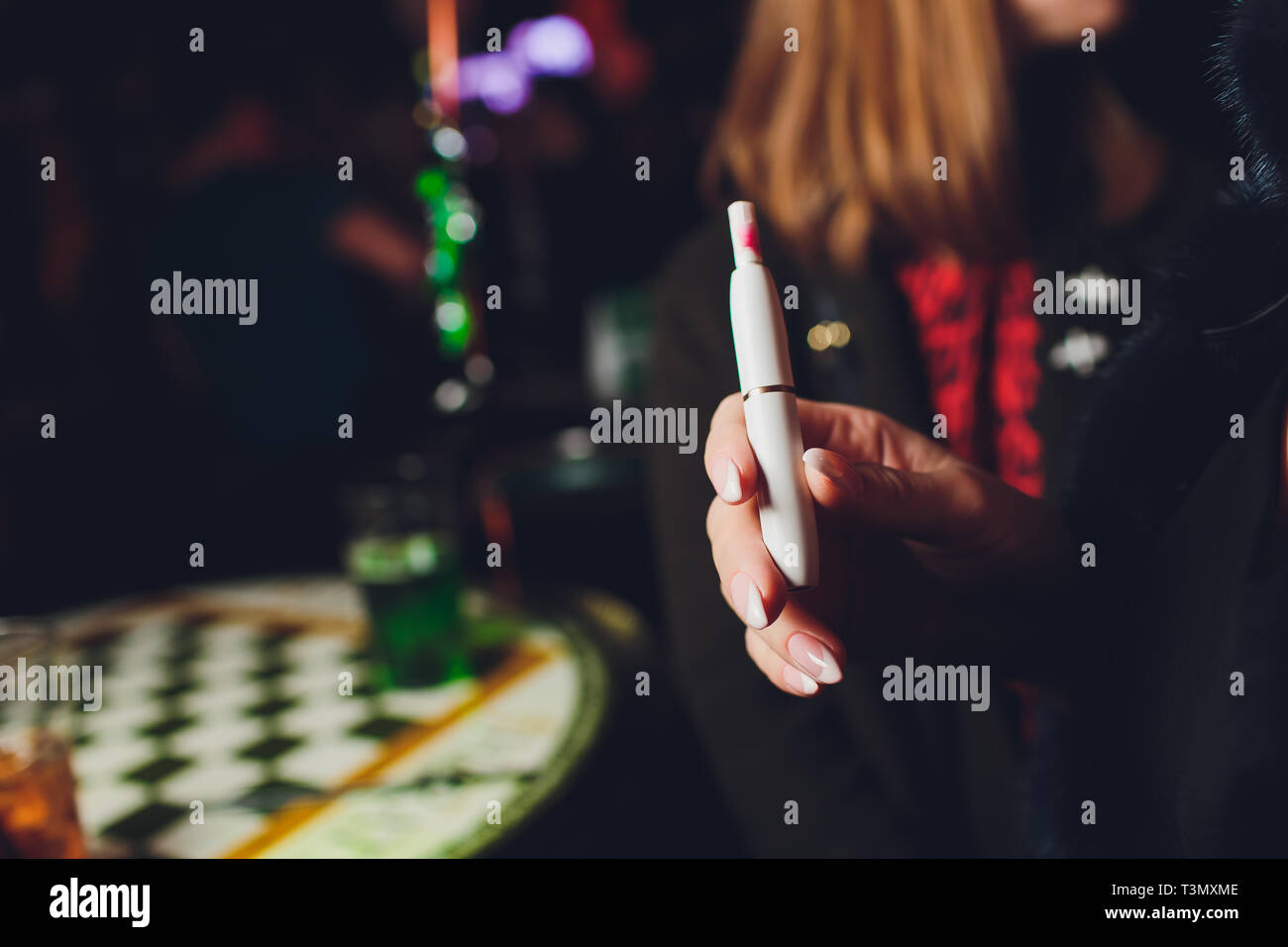 Electronic cigarettes, technology cigarette. Tobacco system IQOS. female hand on blurred background of restaurant Stock Photo