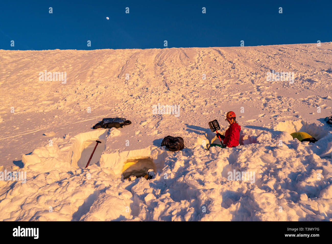 Woman shoveling snow for bivouac camp at sunset Stock Photo