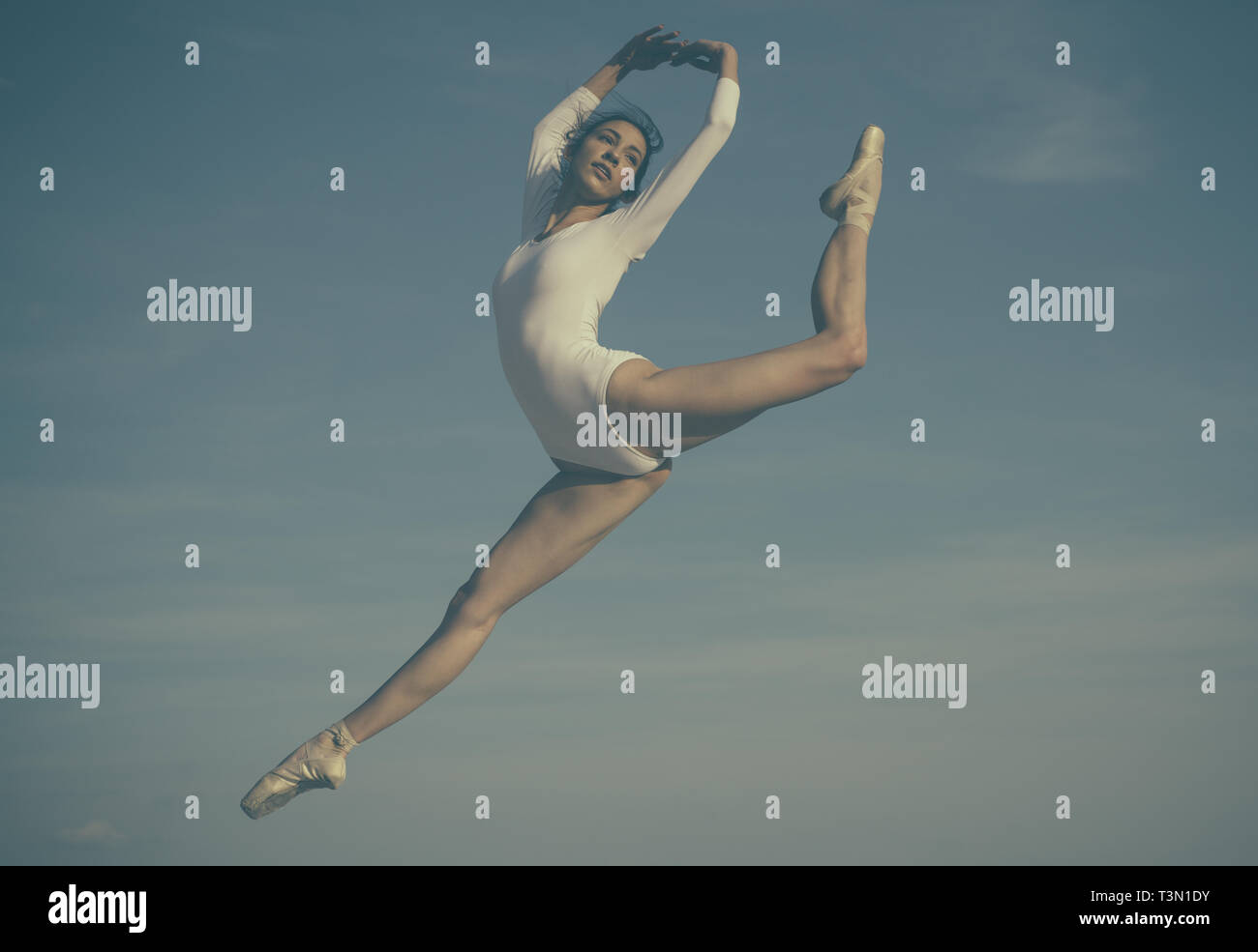 Practicing the art of classical ballet. Young ballerina jumping on blue sky. Pretty woman in dance wear. Cute ballet dancer. Concert performance dance Stock Photo