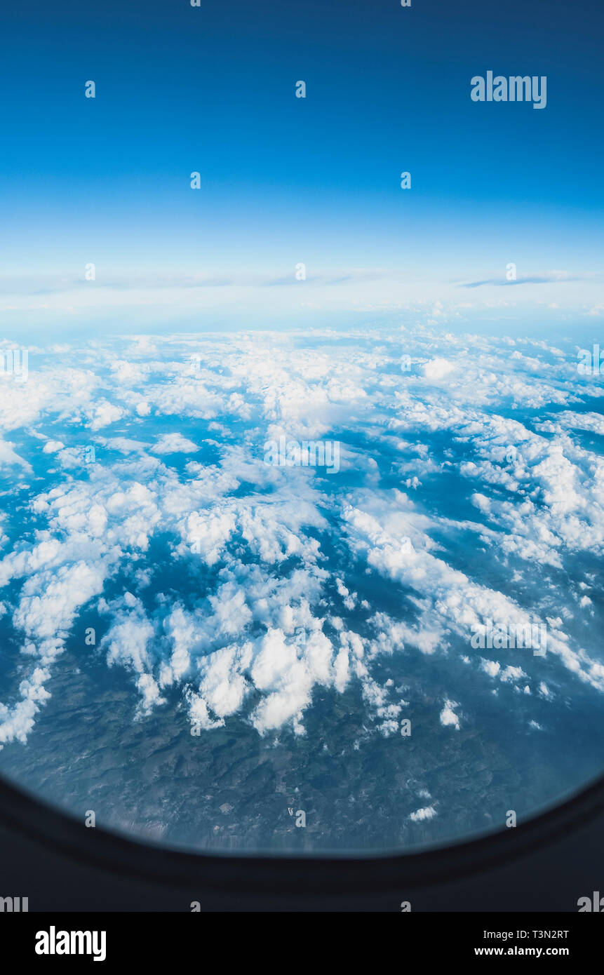 View of the sky above clouds over the earth through the airplane window ...