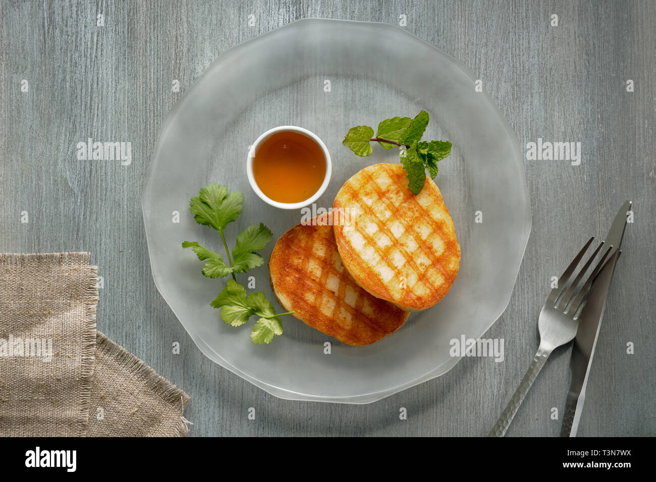 Grilled round slices of Greek cheese with honey, fresh mint and coriander leaves. Flat lay on light grey table. Stock Photo