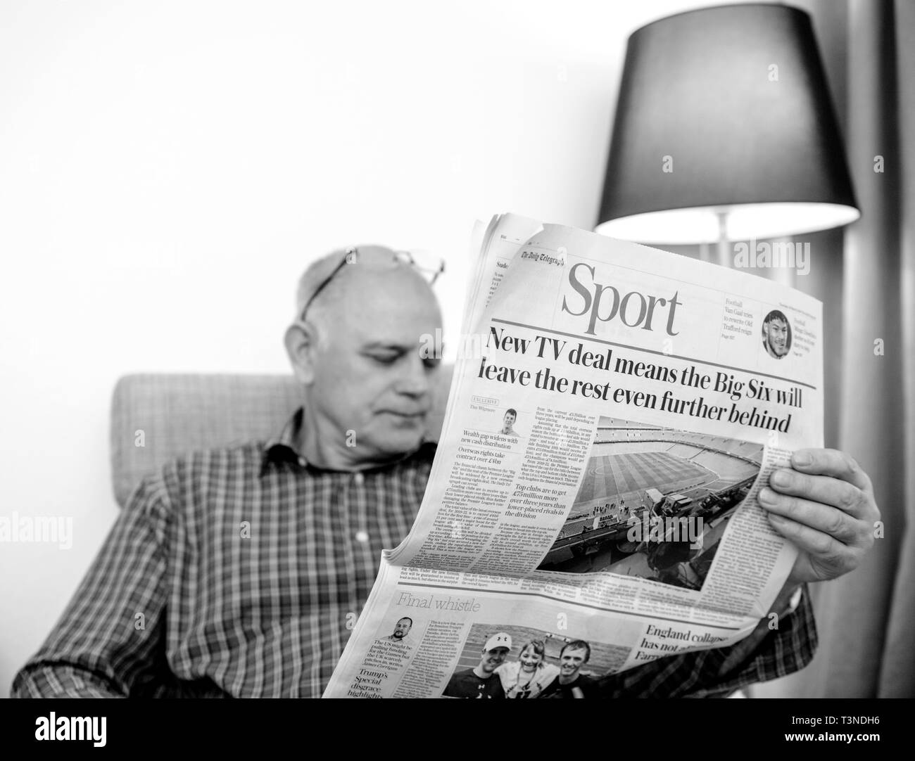 Paris, France - 29 Mar 2019: Senior man reading in living room latest british The Daily Telegraph newspaper UK press Sport section of the newspaper black and white Stock Photo