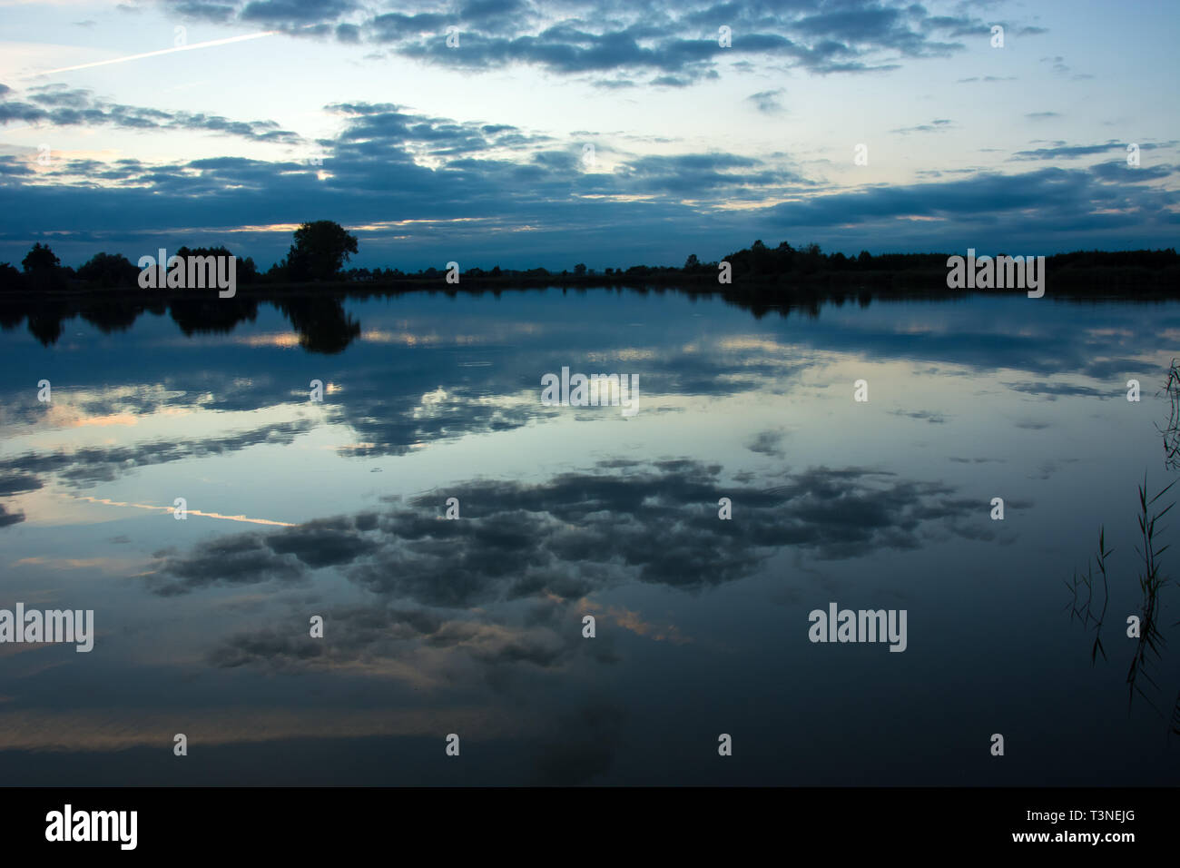 Evening clouds in the blue sky reflecting in the water of a calm lake ...
