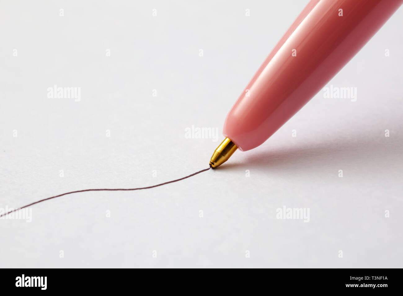A closeup view of a pink ball point pen drawing an ink line on a textured paper surface. Stock Photo